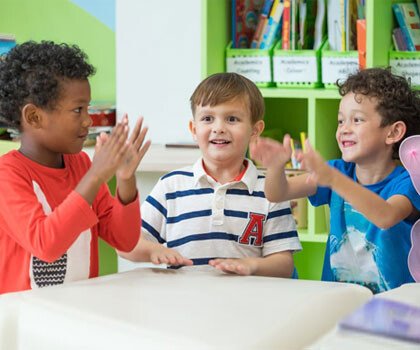 Three young children playing a hand game together at a nursery table