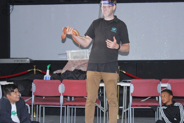 An animal educator introducing a snake to a seated group of children