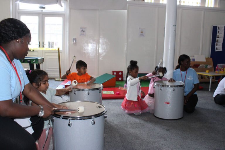 Children playing large drums together in the activity hall