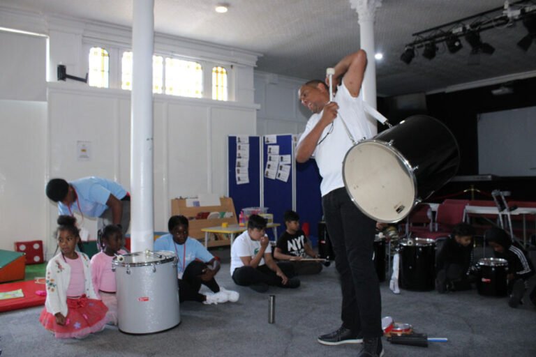 A facilitator demonstrating a large drum to a group of children