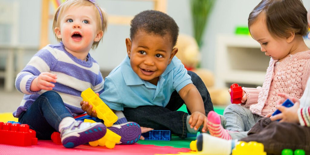 Three toddlers exploring colourful toys together on the floor